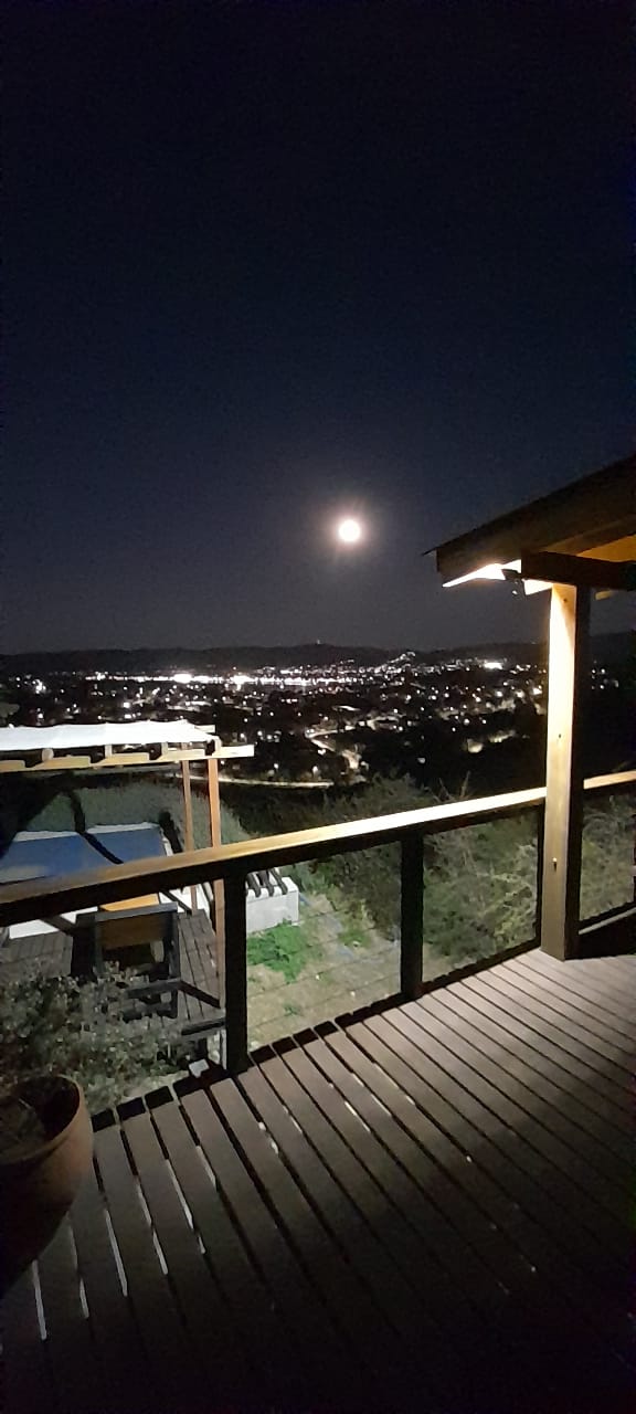 Deck de madera de TORII con vista nocturna a la ciudad iluminada y la luna sobre las sierras